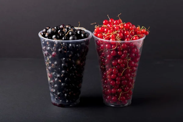 Johannisbeeren in einem Plastikglas auf schwarzem Hintergrund — Stockfoto