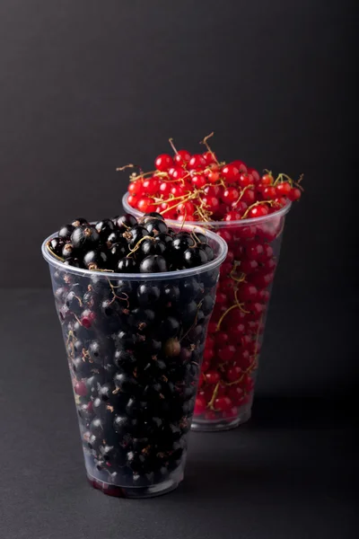 Johannisbeeren in einem Plastikglas auf schwarzem Hintergrund — Stockfoto