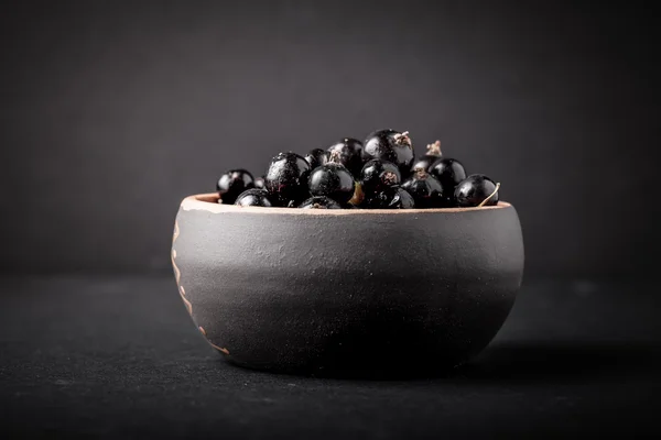 Currant berries in a clay bowl on black background. Selective fo — Stock Photo, Image