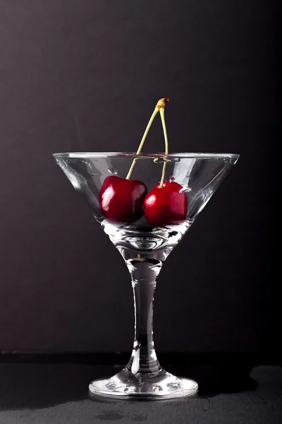 Baies de cerises dans un verre de martini sur fond noir — Photo