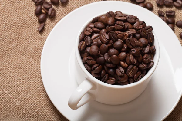 Kaffeebohnen und Kaffee in Tasse auf Büschel. Selektiver Fokus — Stockfoto