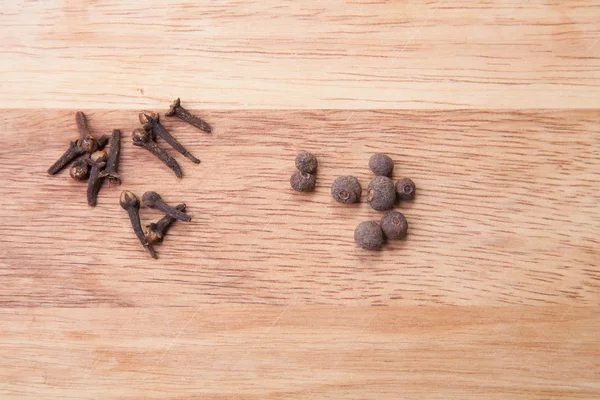 Cloves and black pepper on light wooden cutting board — Stock Photo, Image