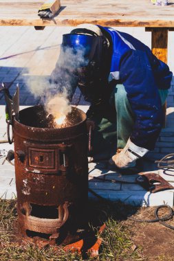 Deneyimli bir kaynakçı. Demir fırınının hazırlık ve kaynak işlemleri. Seçime odaklan. Yüzeyin derinliği. Ayarlanmış.