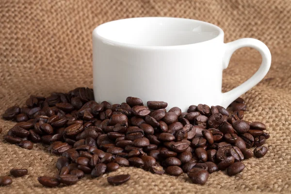 Leere Tasse und geröstete Kaffeebohnen auf Sacktuch — Stockfoto