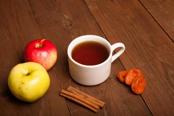 Tazza di tè sul vecchio tavolo di legno con due mele, albicocche secche a — Foto Stock