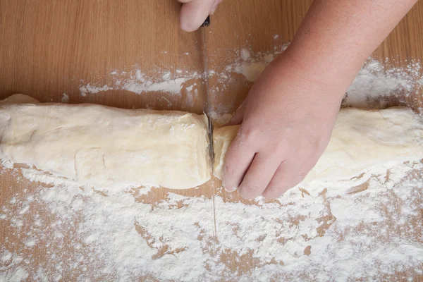 hand with a knife cut dough for rolls