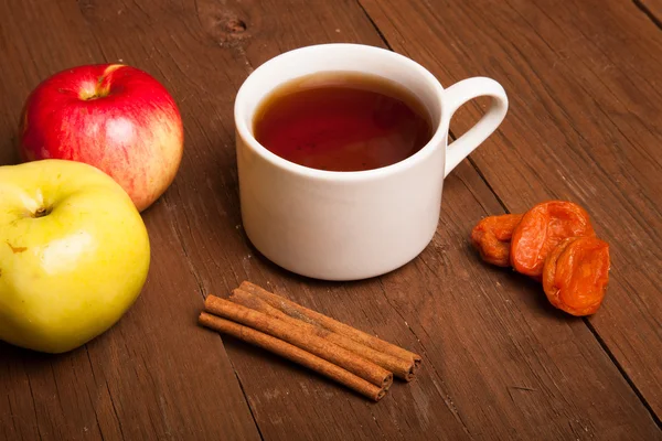 Cup of tea on old wooden table with two apples, dried apricots a — Stock Photo, Image