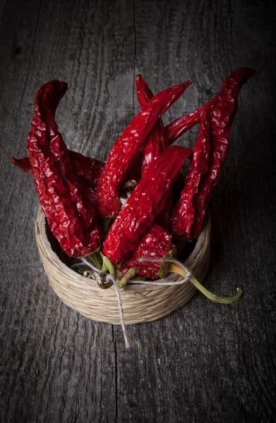 Bunch of red hot peppers lying in a wicker basket on old wooden — Stock Photo, Image