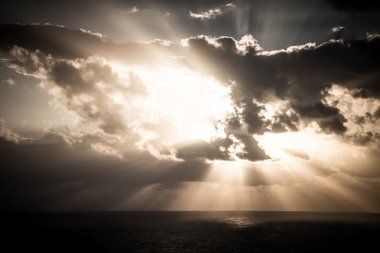 Okyanusun üzerindeki bulutlu karanlık gökyüzünde dramatik gün batımı ışınları