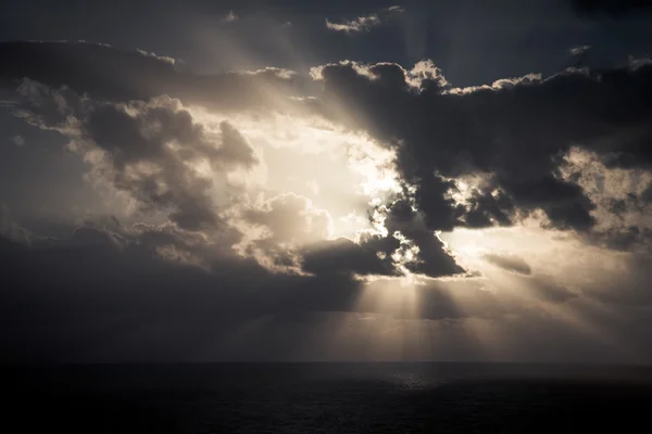 Dramatic sunset rays through a cloudy dark sky over the ocean
