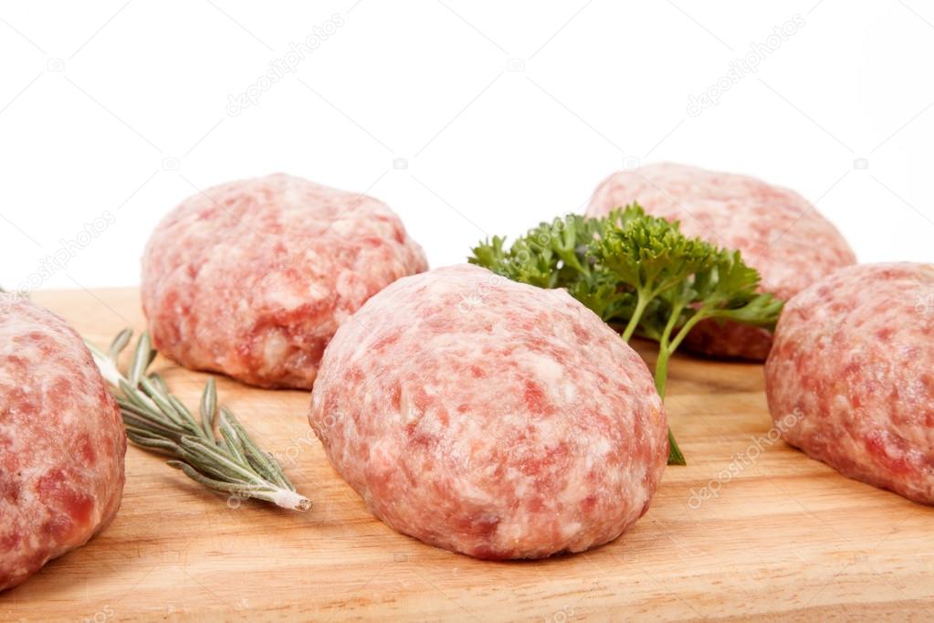 fresh uncooked patties on a wooden board with rosemary and parsl