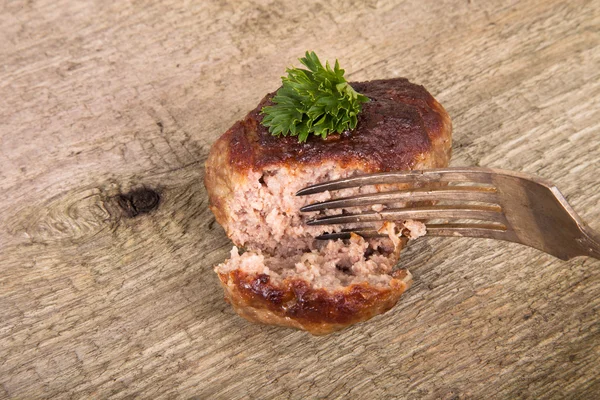 Cutlet and slice on a fork on old wooden table — Stock Photo, Image
