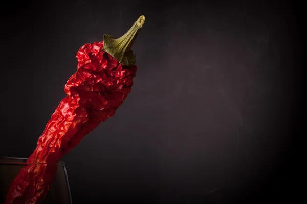 Pimientos rojos picantes en un vaso sobre un fondo oscuro con humo — Foto de Stock