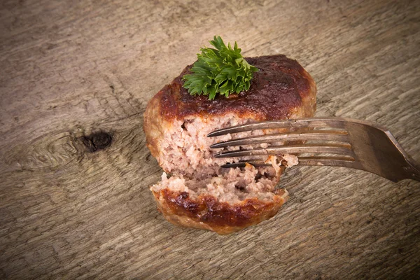 Cutlet and slice on a fork on old wooden table — Stock Photo, Image