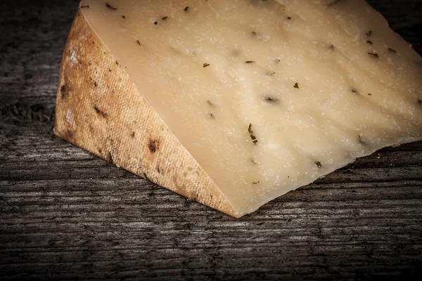 Morceau de fromage à pâte dure avec des herbes sur une vieille table en bois. teinté — Photo