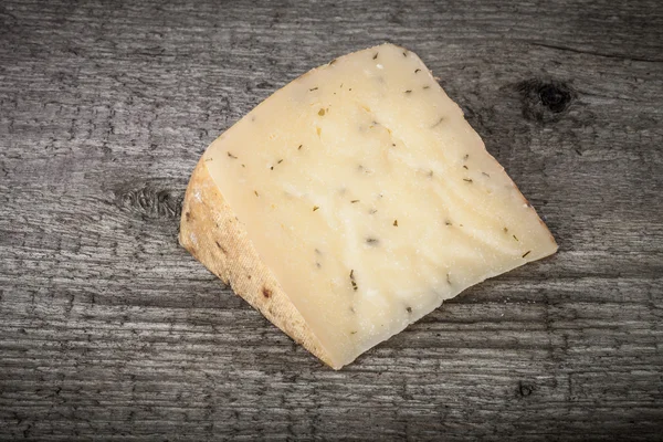 Morceau de fromage à pâte dure avec des herbes sur une vieille table en bois. teinté — Photo