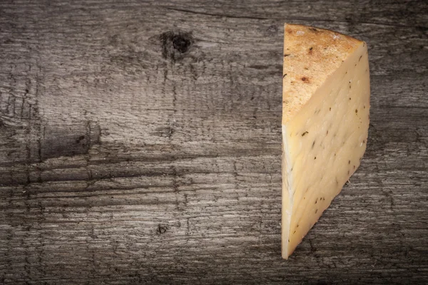 Piece hard cheese with herbs on an old wooden table. Tinted with — Stock Photo, Image