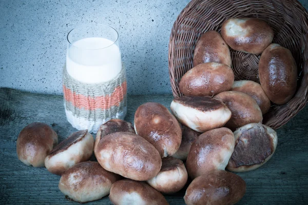 Tortas com carne ou repolho em uma cesta de vime e um copo de leite — Fotografia de Stock