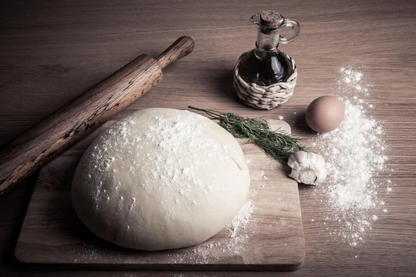 Pâte sur une planche avec de la farine. huile d'olive, oeufs, rouleau à pâtisserie, garli — Photo