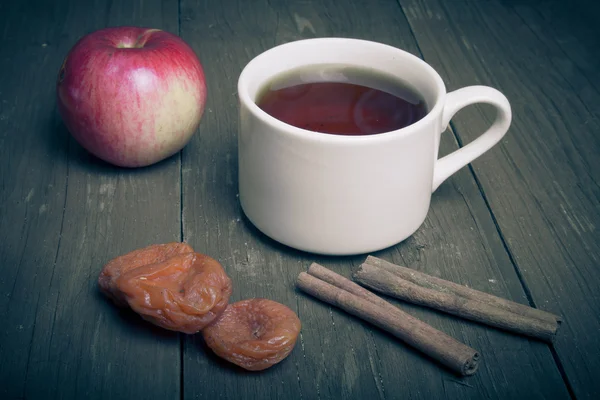 Taza de té sobre una vieja mesa de madera con dos manzanas, albaricoques secos a — Foto de Stock
