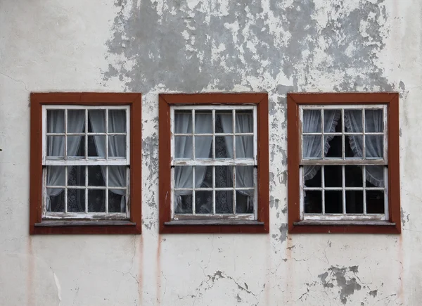 Three windows on the shabby wall closed with curtains — Stock Photo, Image