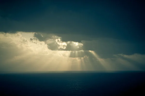 Dramatic sunset rays through a cloudy dark sky over the ocean — Stock Photo, Image