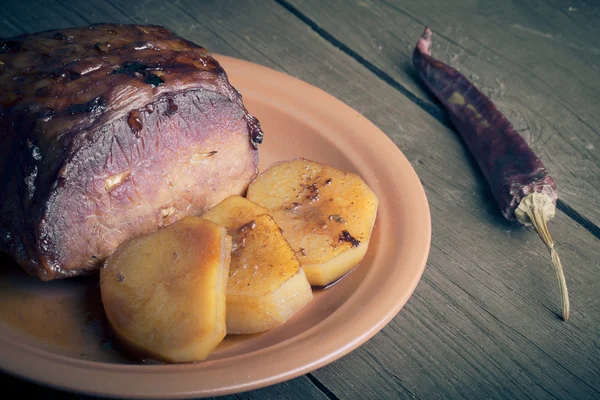 Piece of pork, peppers and potatoes in an old wooden table — Stock Photo, Image