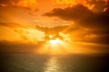 Okyanusun üzerindeki bulutlu karanlık gökyüzünde dramatik gün batımı ışınları 