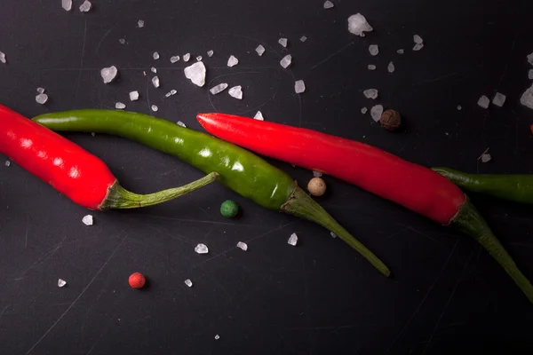 Czerwone i zielone chili peppers, grubej soli na tablicy. odcień — Zdjęcie stockowe