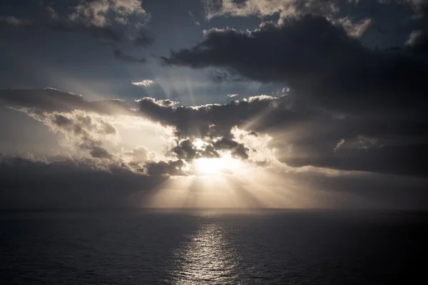 Dramatický západ slunce paprsky přes zataženou tmavou oblohu nad oceánem — Stock fotografie