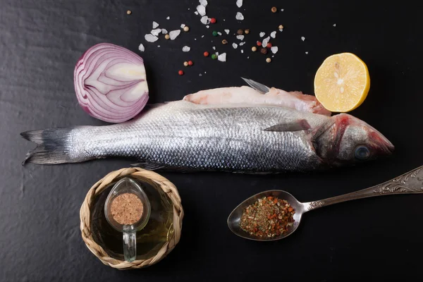 Taze deniz balığı koyu arka plan üzerinde baharatlarla yalan.