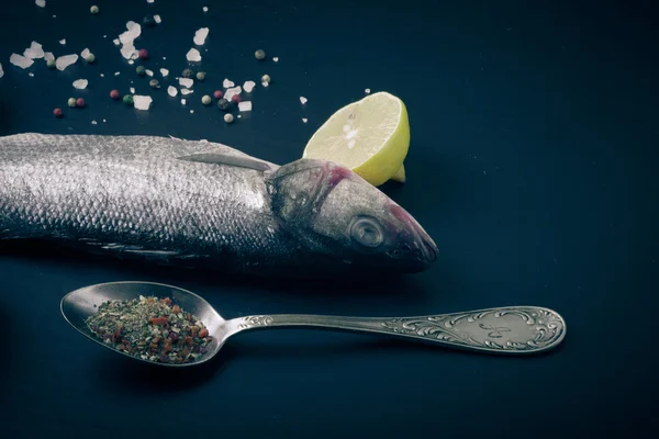 Fresh sea fish lying on dark background with spices. — Stock Photo, Image