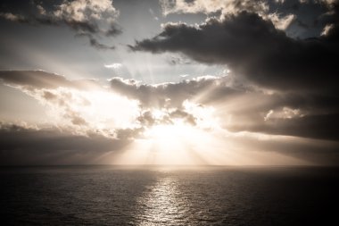 Okyanusun üzerindeki bulutlu karanlık gökyüzünde dramatik gün batımı ışınları 