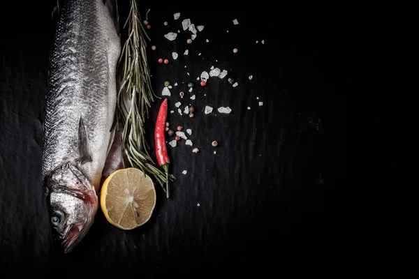 Fresh sea fish lying on dark background with spices. Space for t — Stock Photo, Image