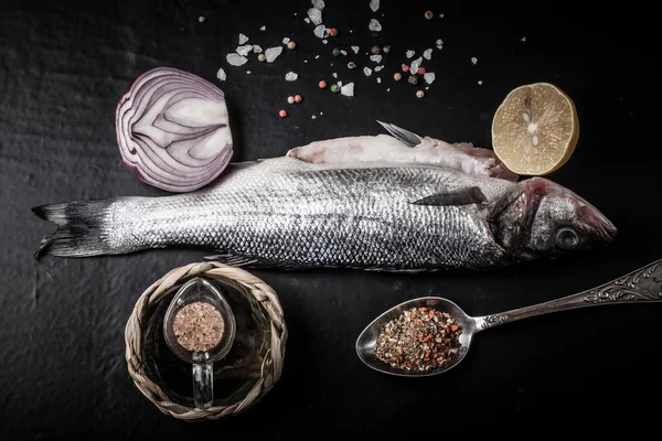 Peixe-marinho fresco deitado no fundo escuro com especiarias — Fotografia de Stock