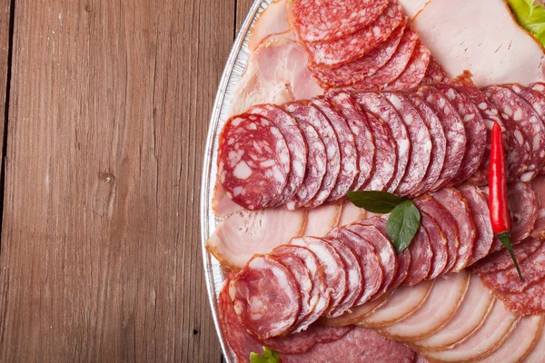 Teller mit verschiedenen Wurstscheiben auf einem alten Holztisch. mit — Stockfoto