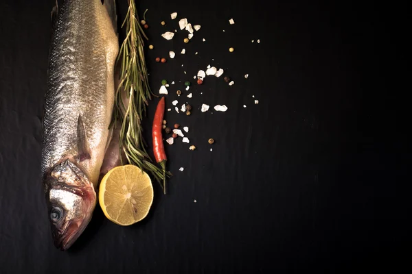 Fresh sea fish lying on dark background with spices. Space for t — Stock Photo, Image