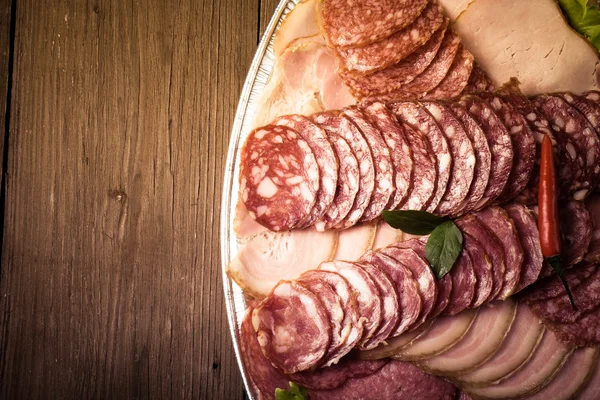 Plate with different sliced sausage on an old wooden table. With — Stock Photo, Image