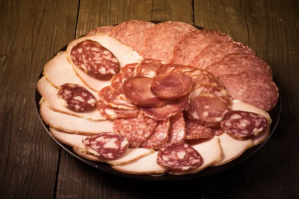 Plate with different sliced sausage on an old wooden table — Stock Photo, Image