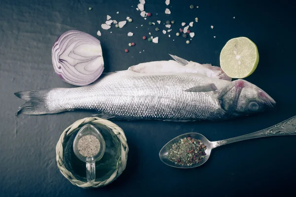 Fresh sea fish lying on dark background with spices. tinted — Stock Photo, Image