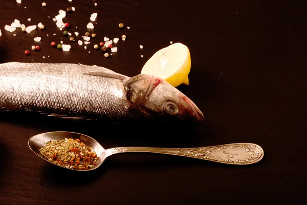 Fresh sea fish lying on dark background with spices. — Stock Photo, Image