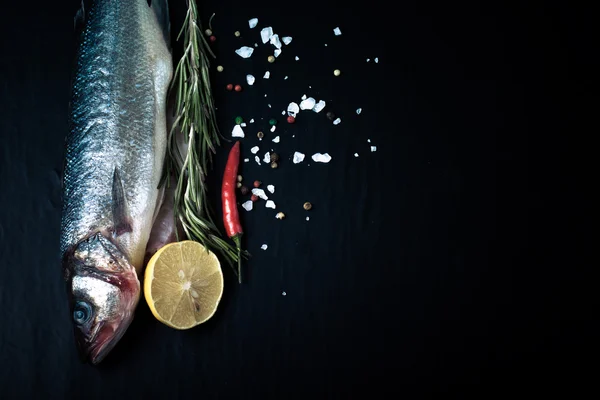 Fresh sea fish lying on dark background with spices. Space for t — Stock Photo, Image