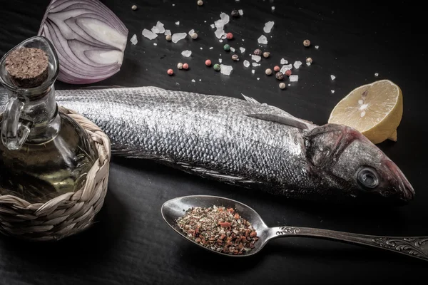 Fresh sea fish lying on dark background with spices. — Stock Photo, Image