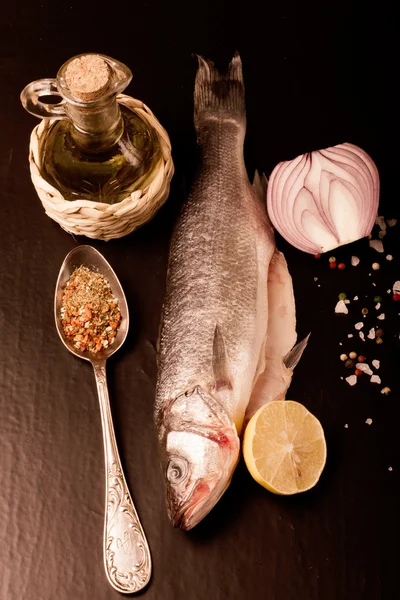 Fresh sea fish lying on dark background with spices. tinted — Stock Photo, Image