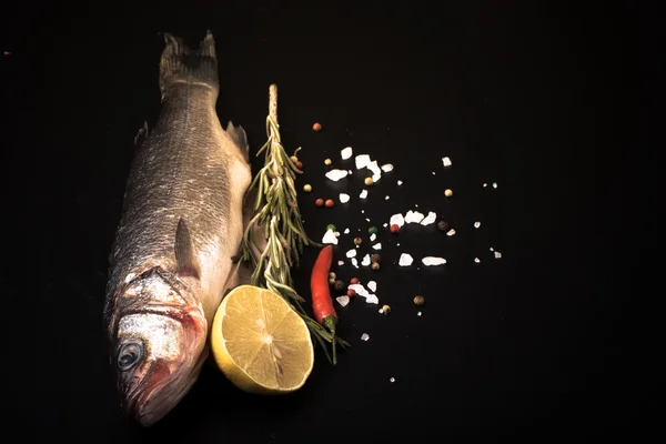 Fresh sea fish lying on dark background with spices. Space for t — Stock Photo, Image