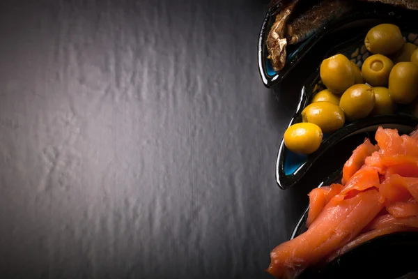 Fish assortment and olives on a plate on a dark background. With — Stock Photo, Image