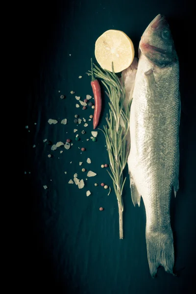 Fresh fish, lemon, pepper and rosemary on a black background. Ti — Stock Photo, Image