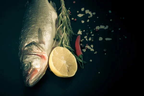 Frischer Fisch, Zitrone, Pfeffer und Rosmarin auf schwarzem Hintergrund. ti — Stockfoto
