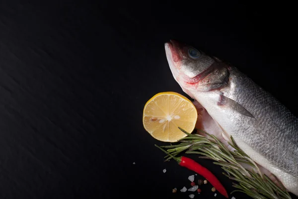 Frischer Fisch, Zitrone, Pfeffer und Rosmarin auf schwarzem Hintergrund. ti — Stockfoto