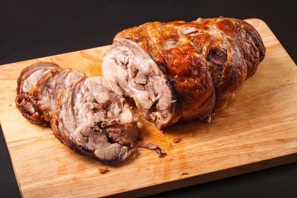 Rotolo di maiale al forno su una tavola di legno su uno sfondo scuro . — Foto Stock